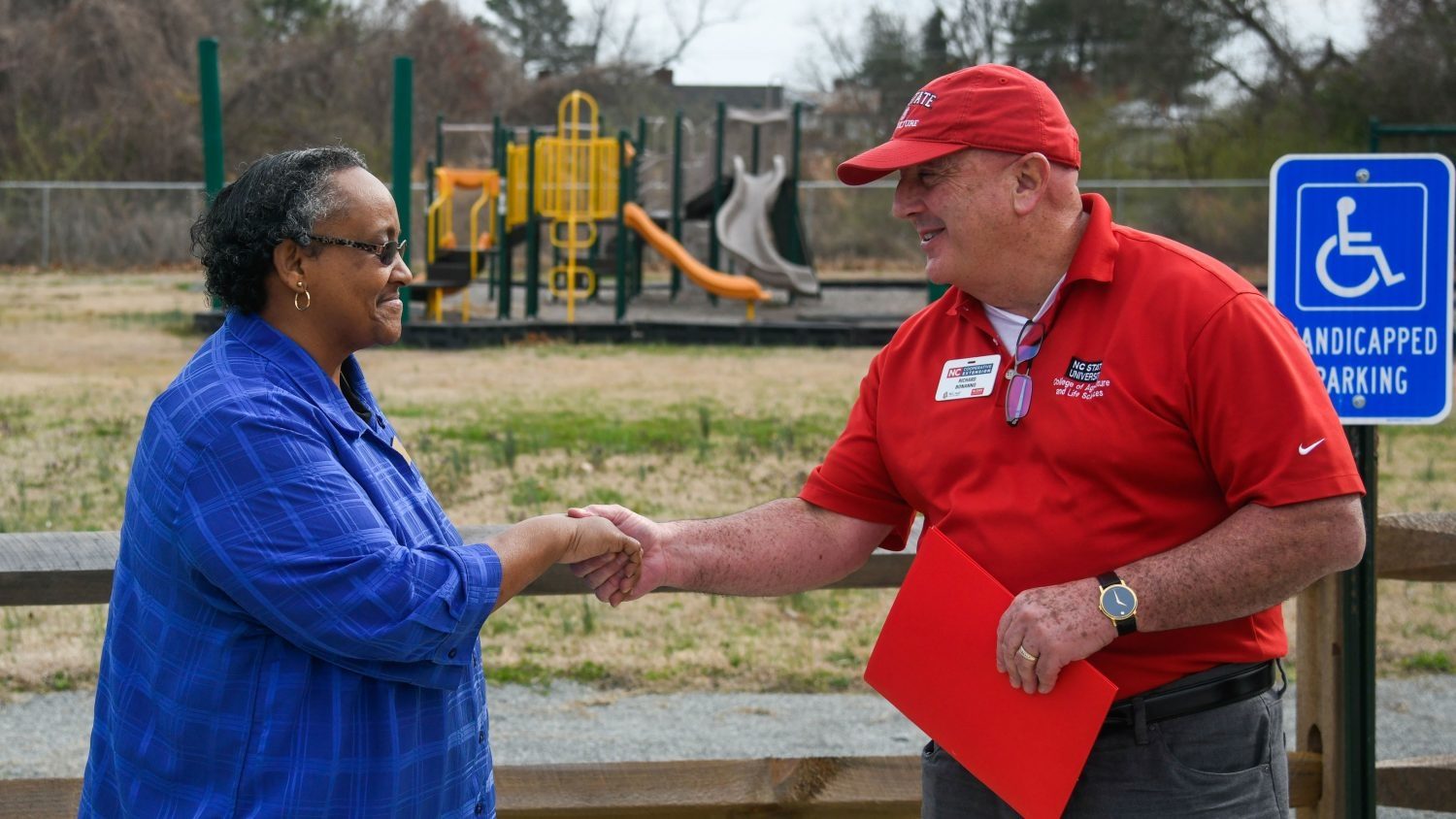 Two people shake hands. Playground equipment behind them.
