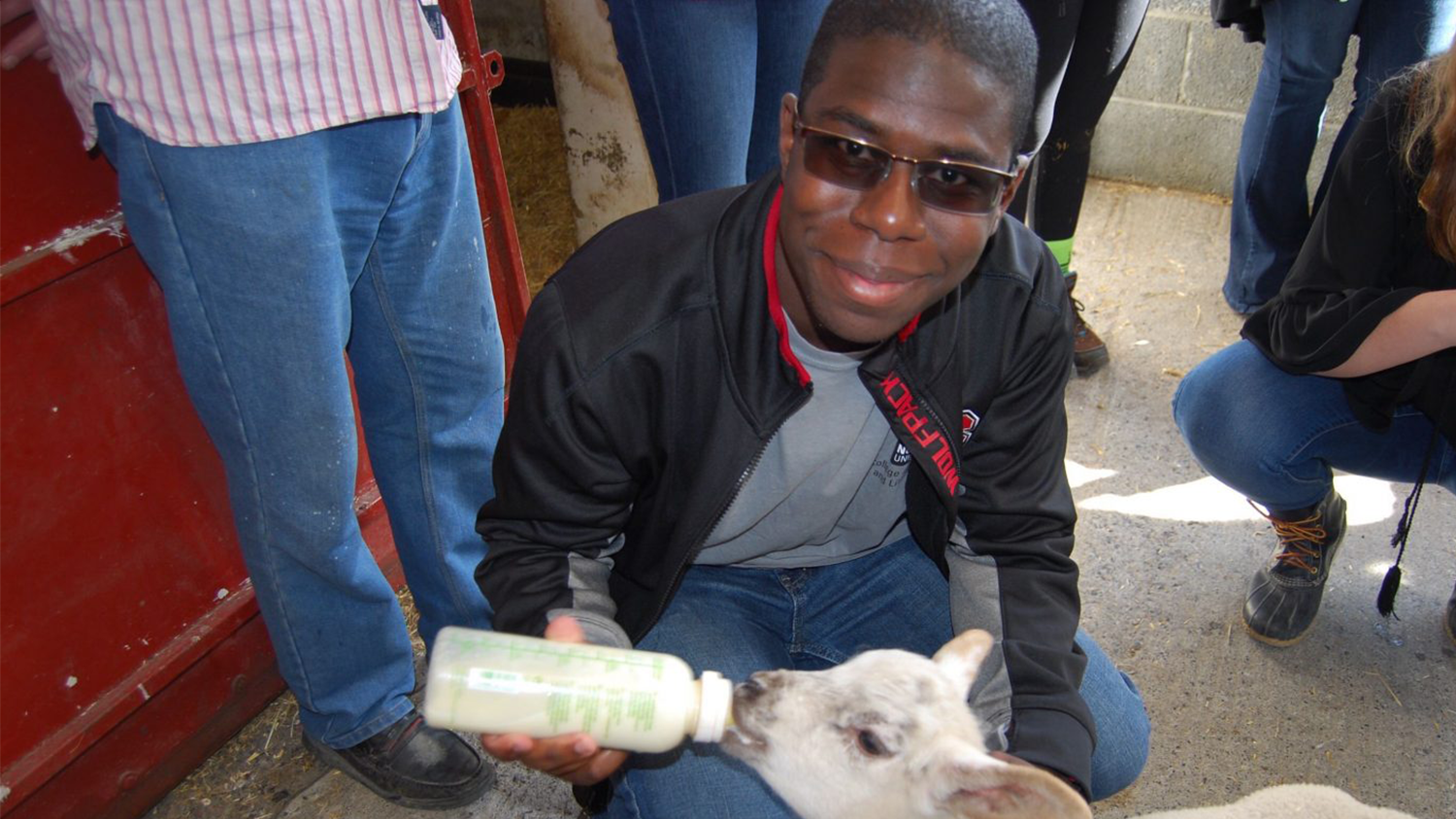 Black male student feeding a goat a bottle
