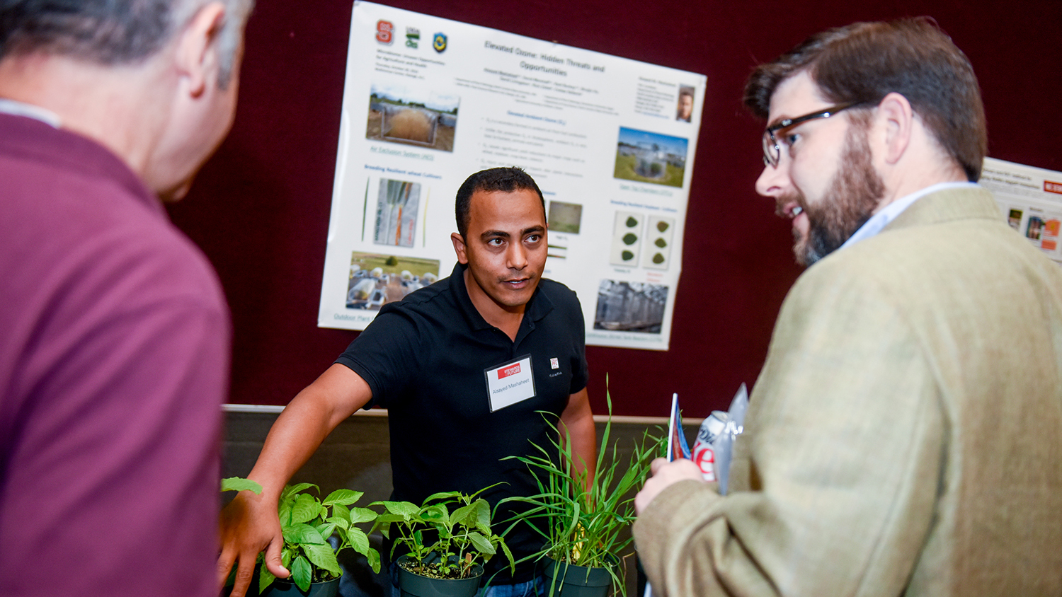 Scientist with plants explaining research to two onlookers.