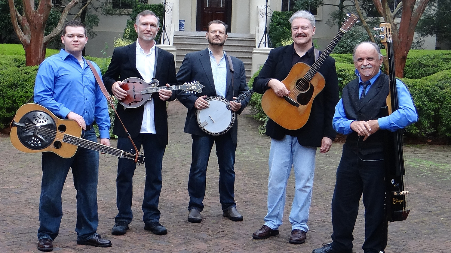 Four men standing outside and holding bluegrass instruments.