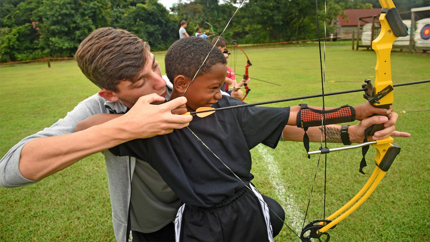 Young Caucasian male helping young African American boy with archery