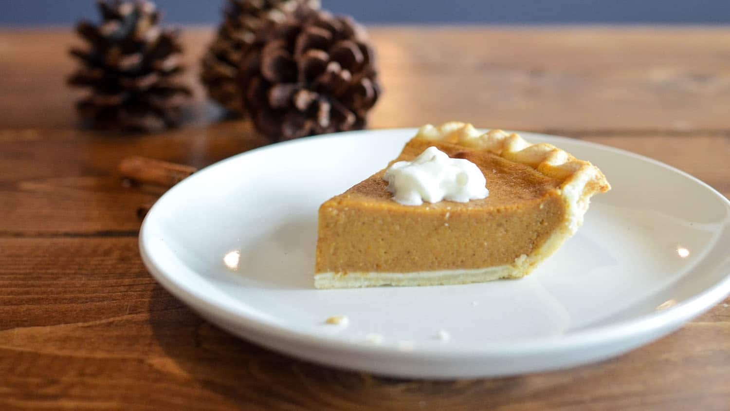 a slice of pumpkin pie sits on a white plate on a wooden table