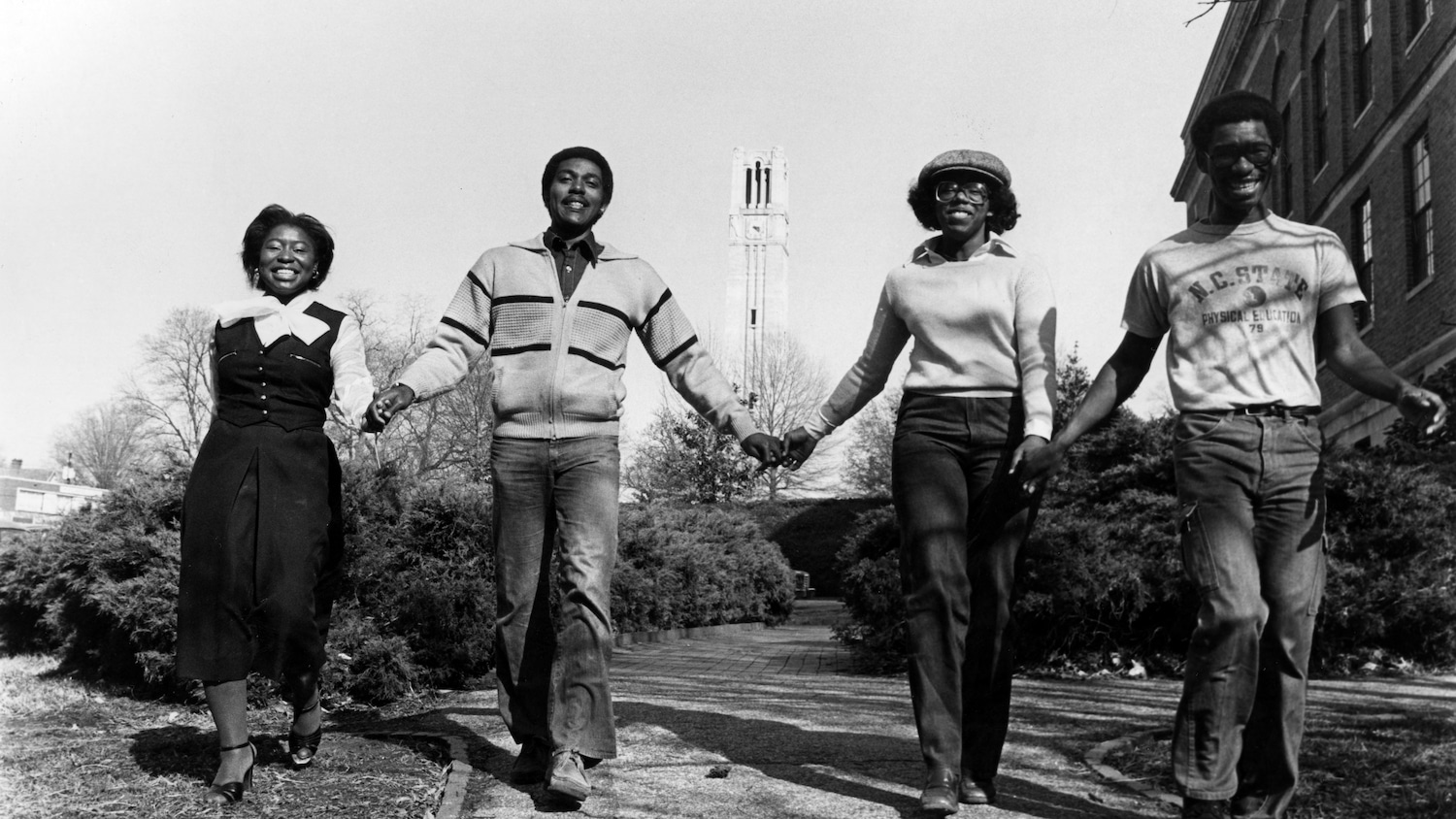 Black and white photograph of African American students holding hands with the Belltower behind them.