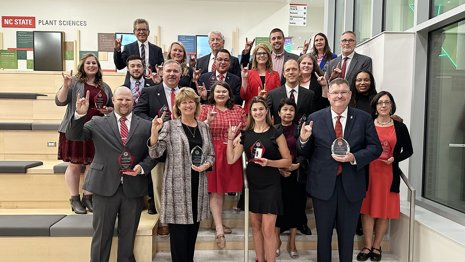 a group of people holding award plaques and doing the wolfpack hand sign