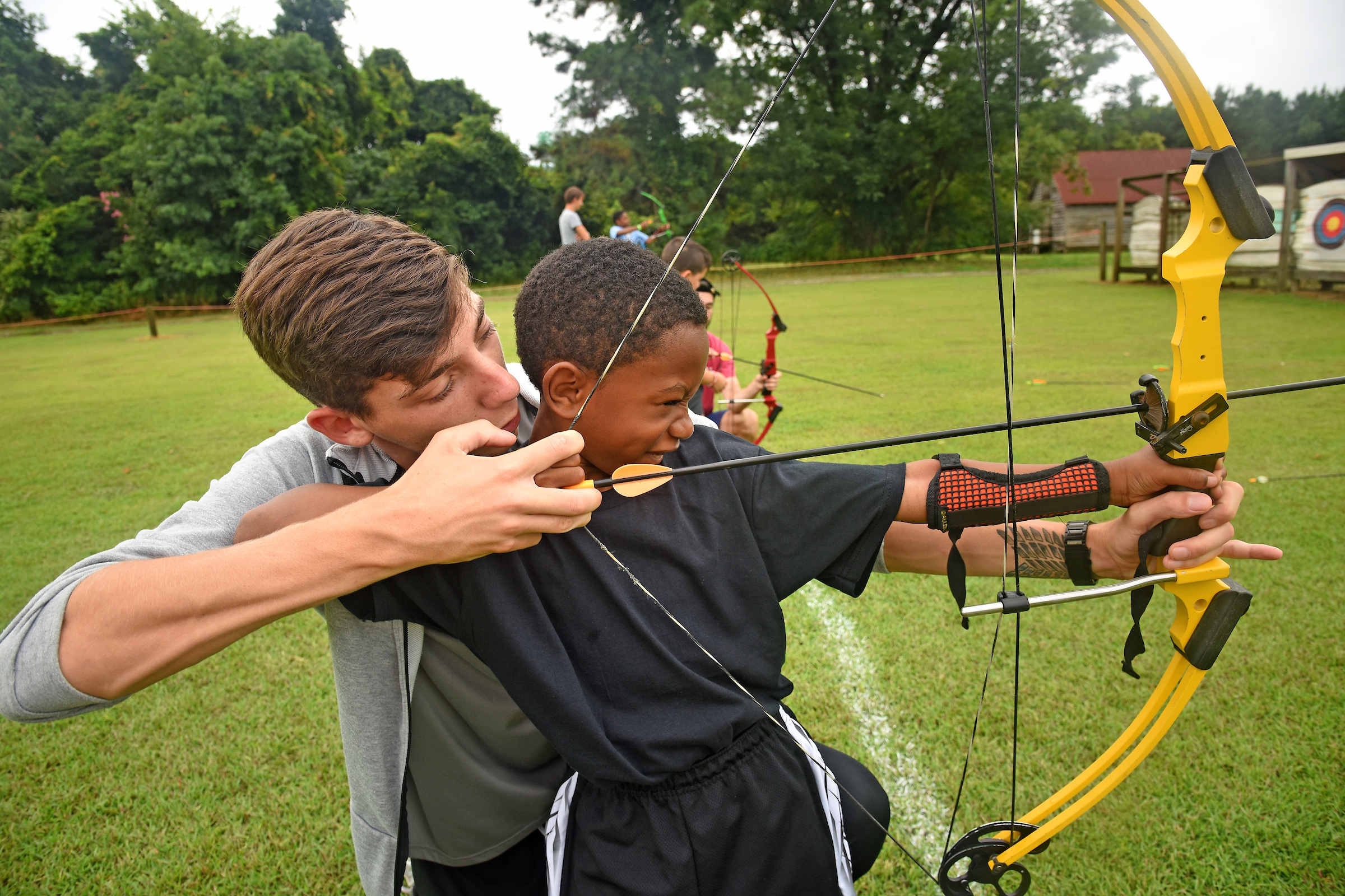 Eastern 4-H Camp counselor assists a camper with his aim during an archery session.