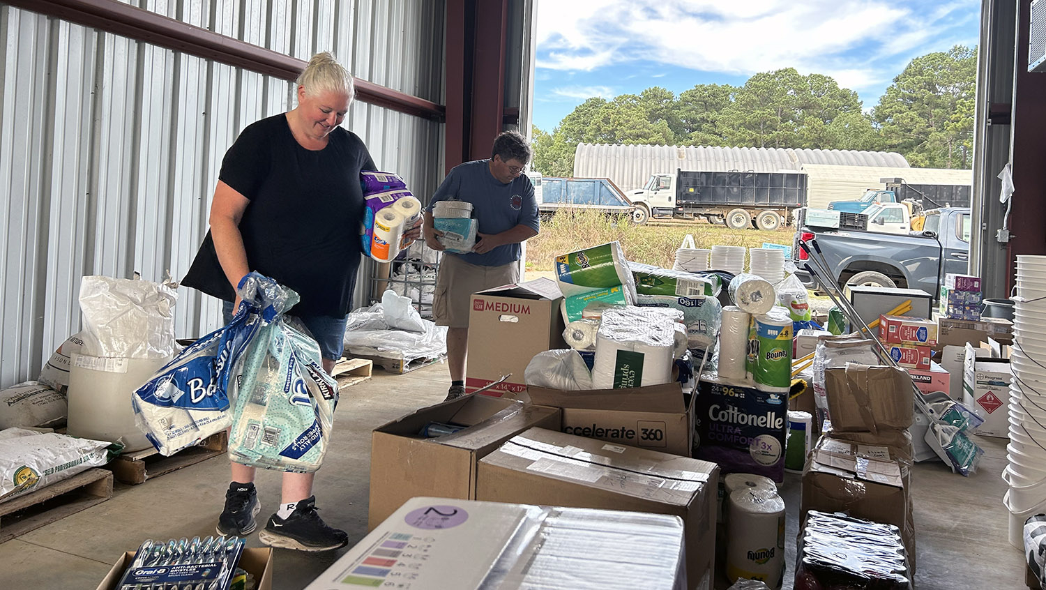 a woman and man organize supplies including toilet paper, paper towels and dry food.