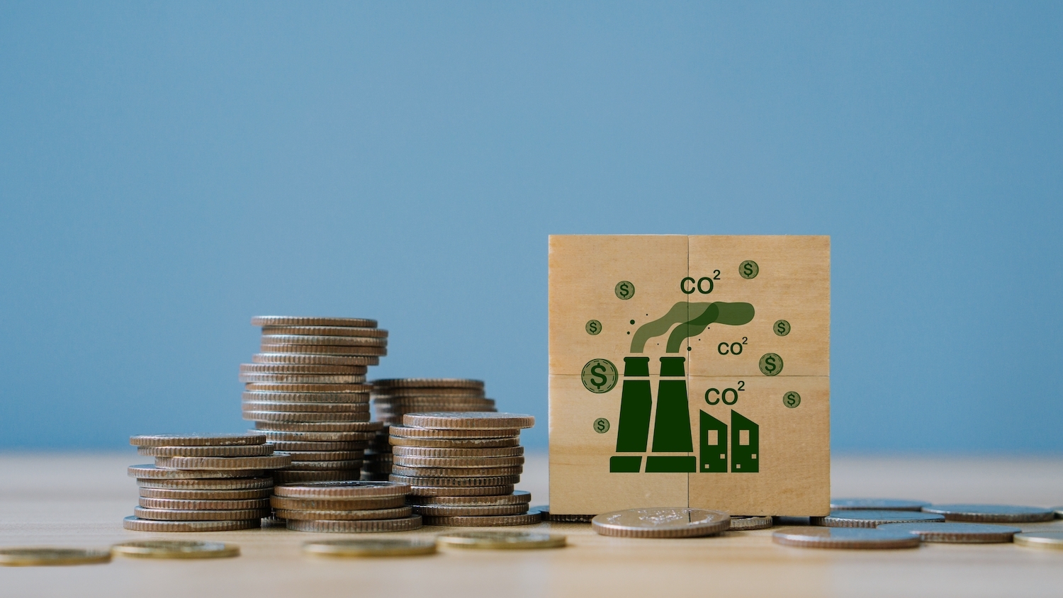 A stack of coins and a wooden tile with a drawing of smokestacks illustrate the idea of greenhouse emissions taxes.
