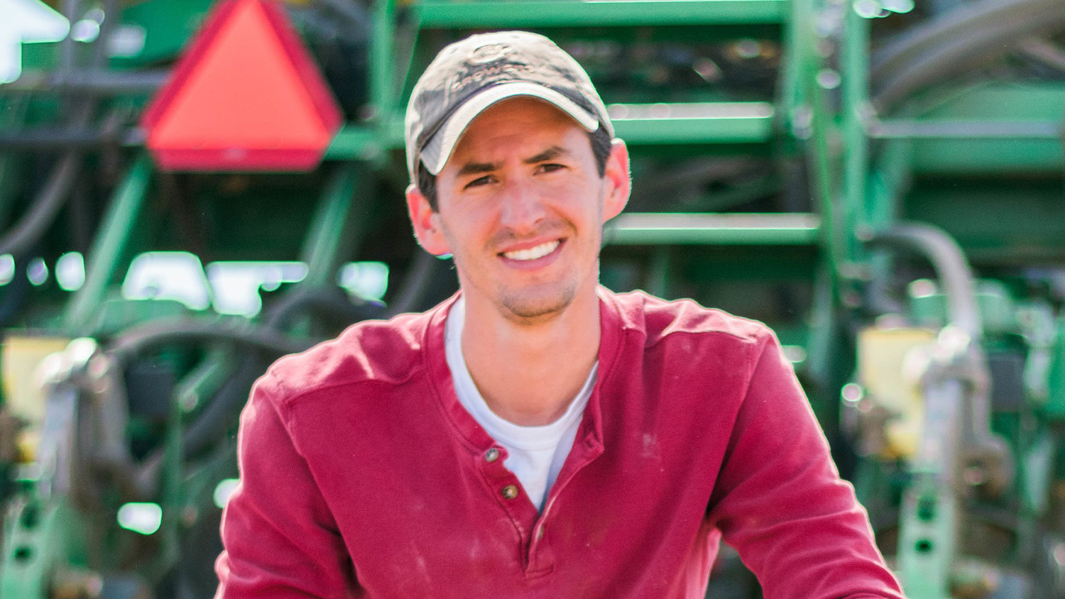 Man in ball cap in front of tractor.