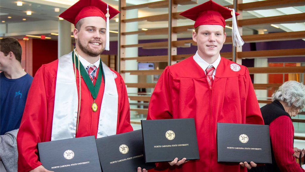 two AGI students standing with their diplomas.