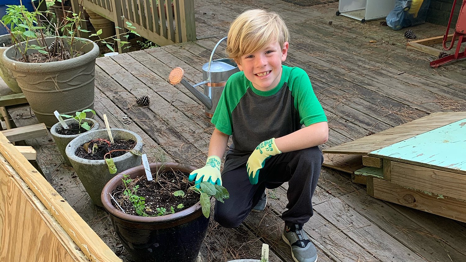 Child on outdoor deck posing with his container garden