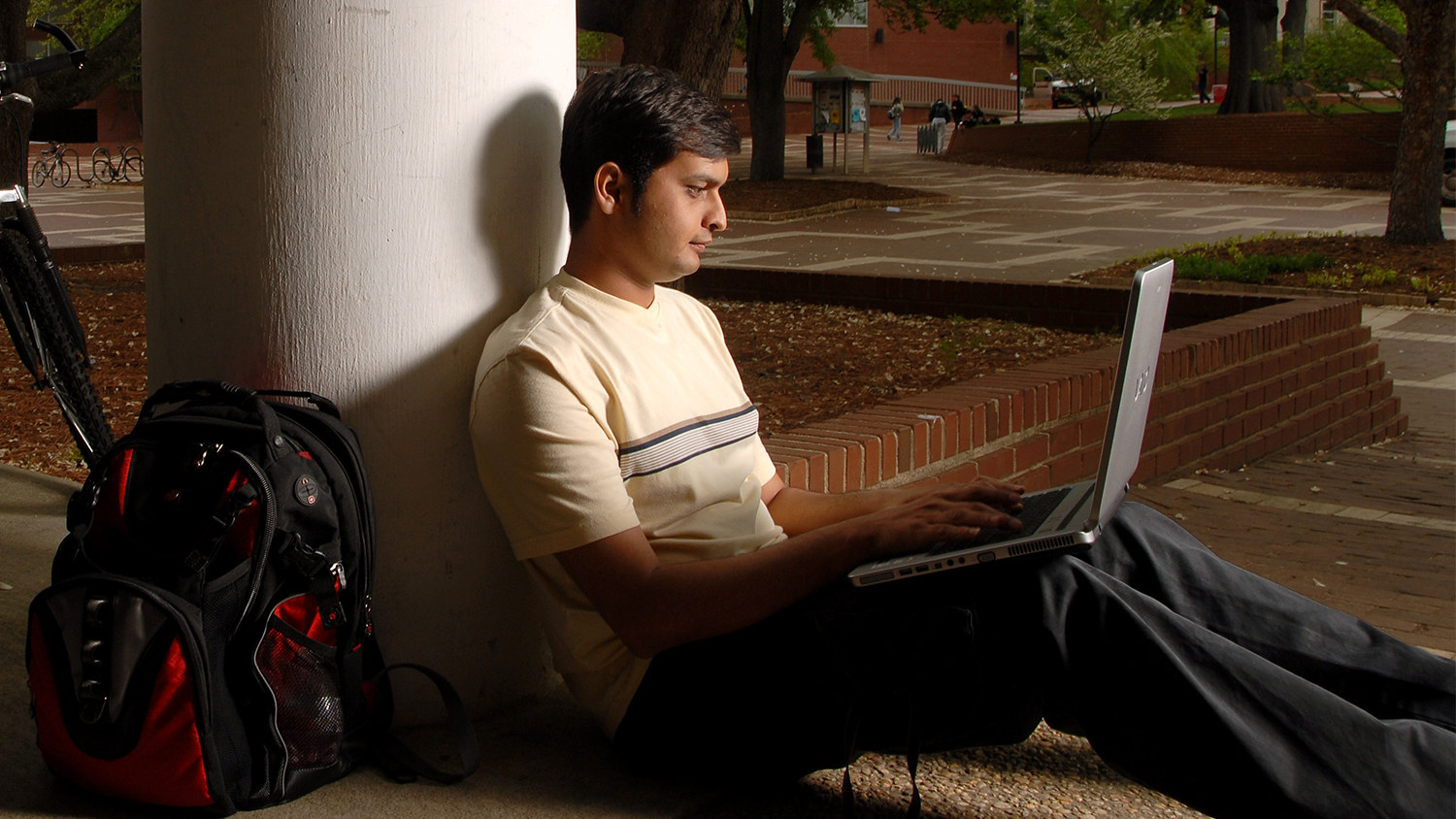 student sitting on brickyard on a laptop.
