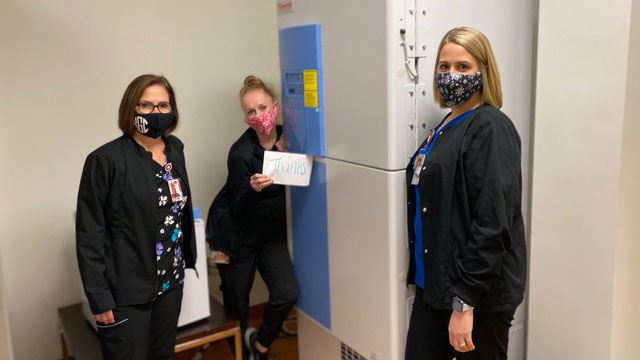 Three female nurses standing next to a freezer.