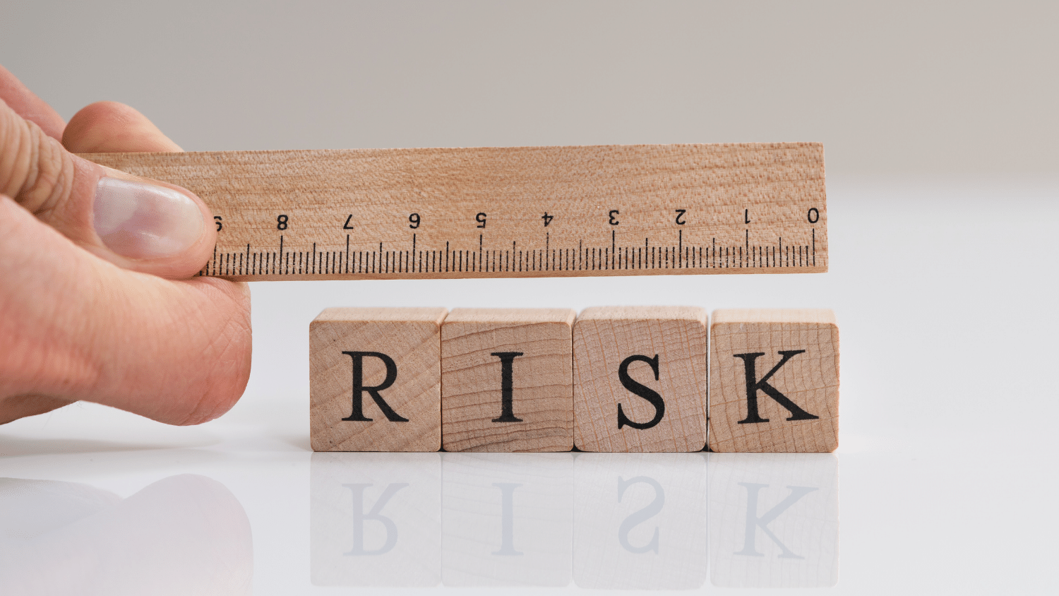 A hand holding a ruler over wooden blocks spelling the word "risk."