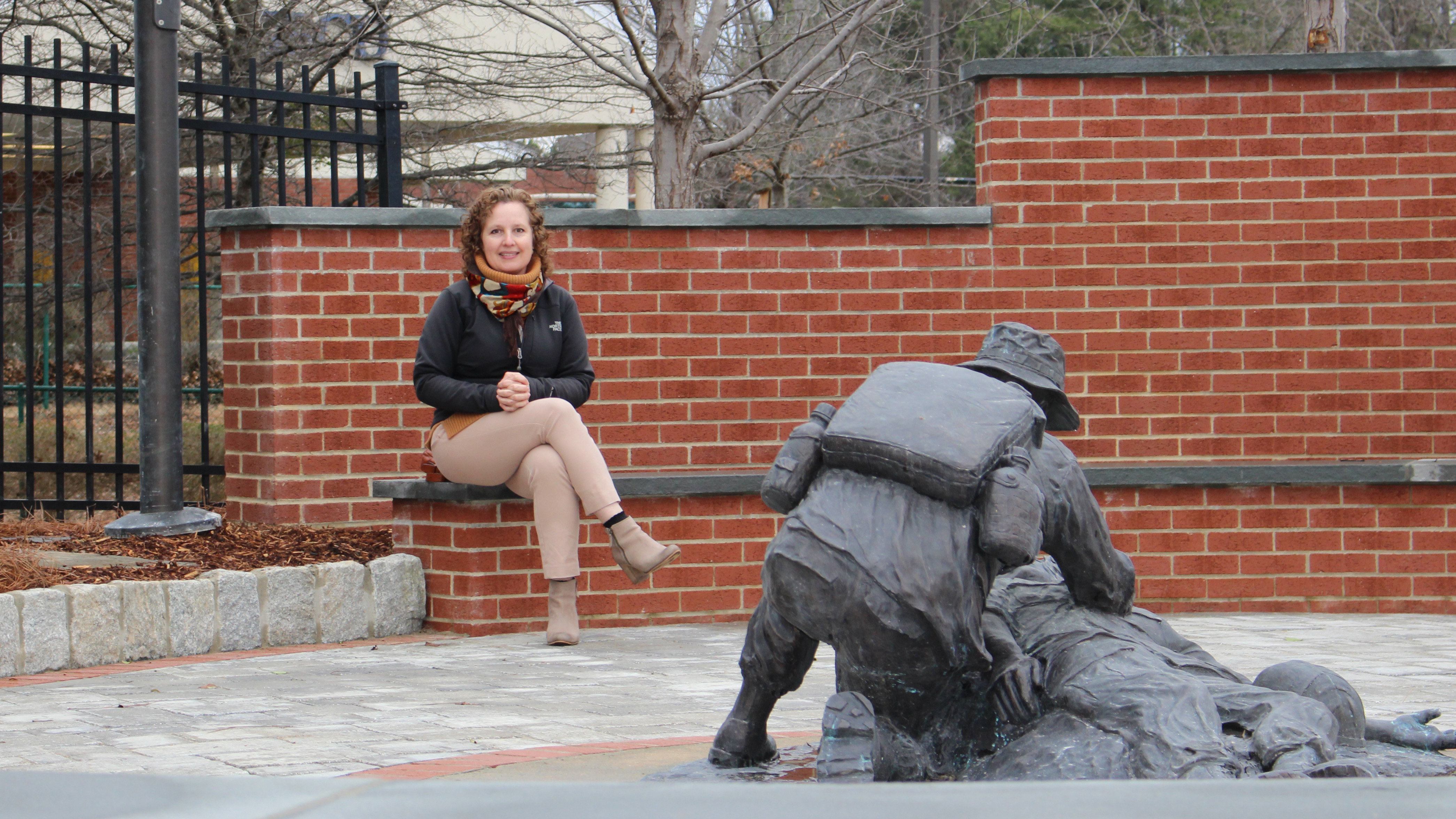 Julieta Sherk seated in a patio. In the foreground: a statue of a medic aiding a wounded soldier.