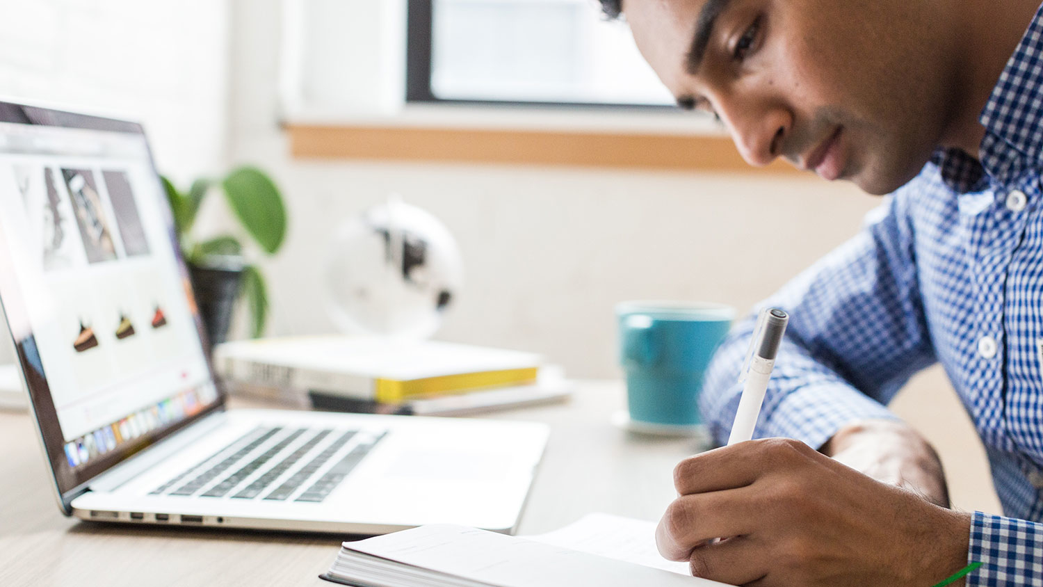 Young man taking notes and working on laptop