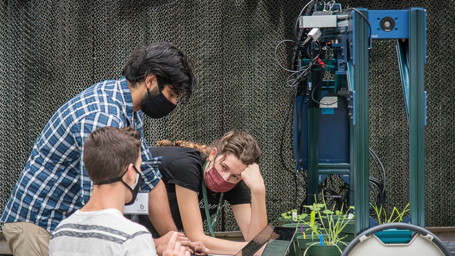 Three students work together over a greenhouse robot.