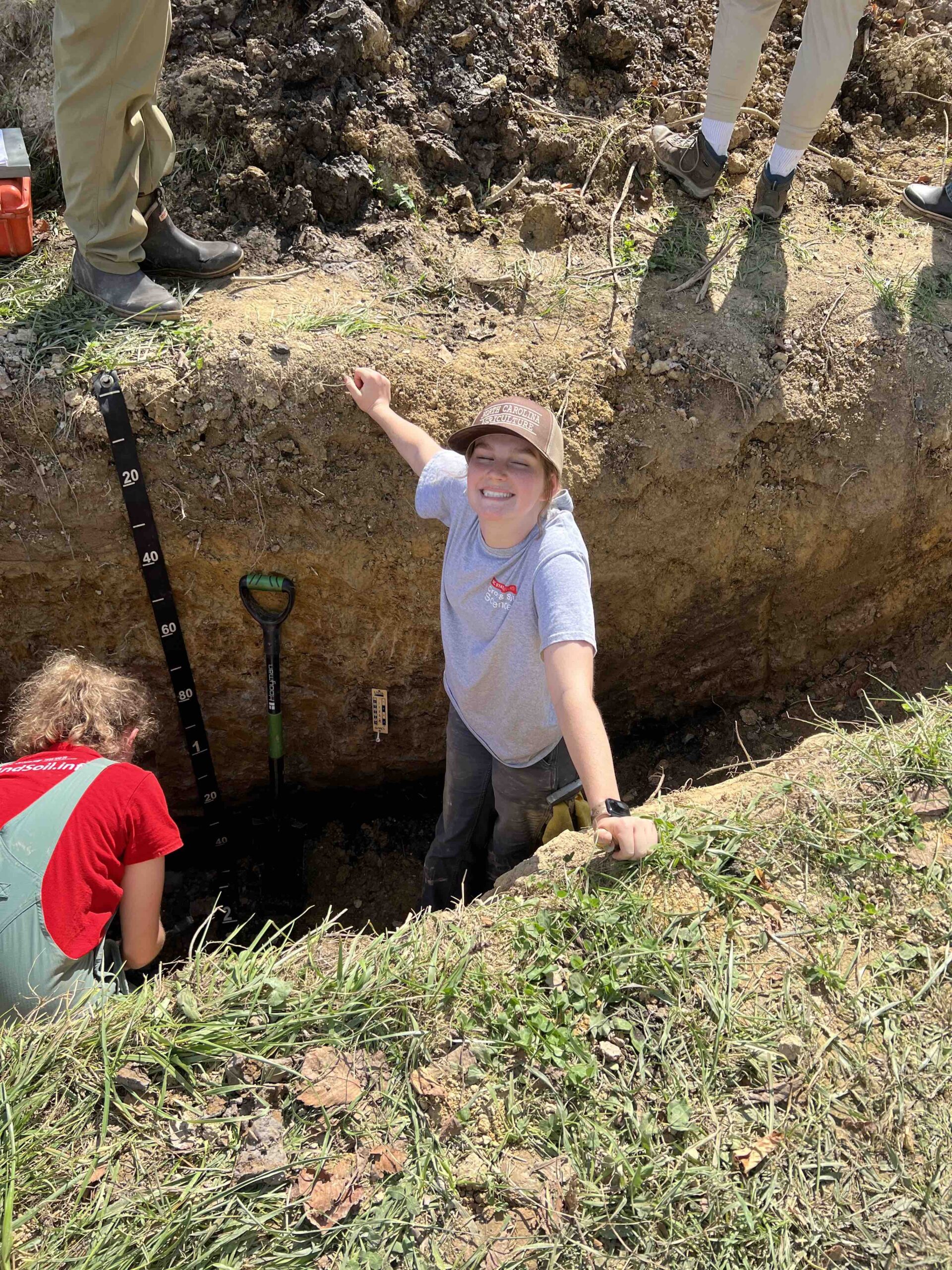 Sarah Bailey smiles up from a soil judging pit at the 2023 Eastern Collegiate Soil Judging competition