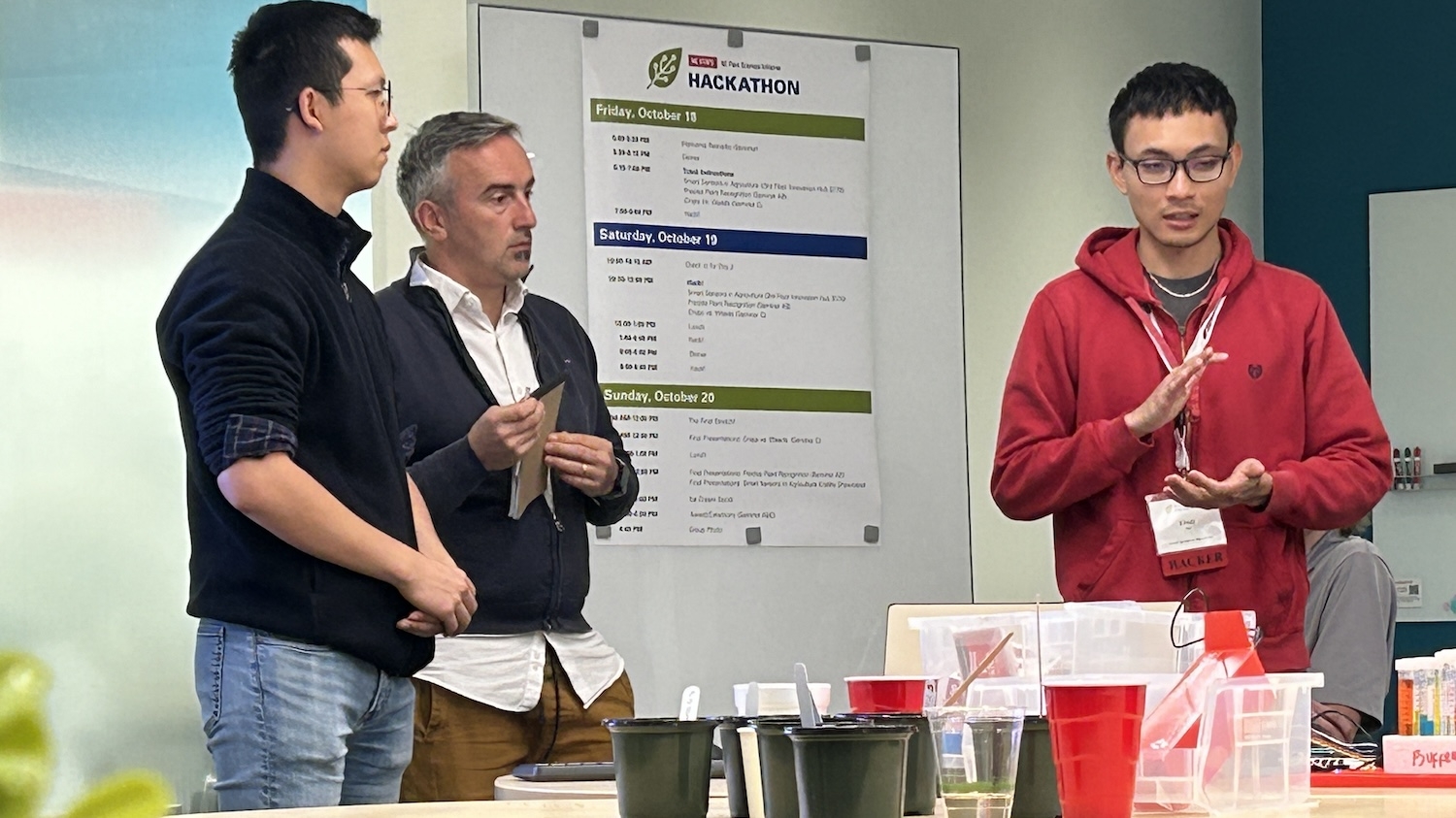 Three people making a presentation in front of a poster that says "Hackathon"