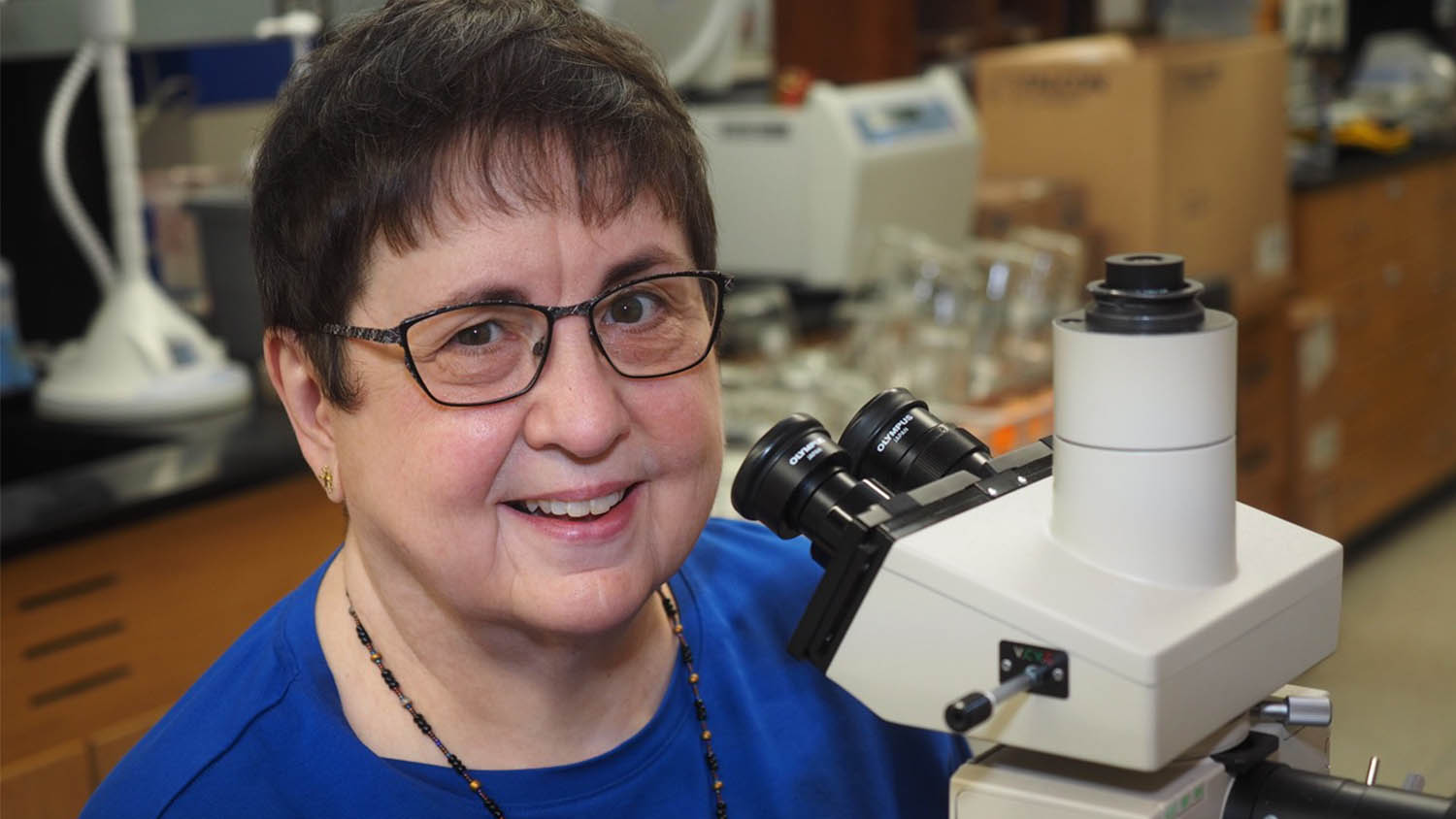 Woman in blue shirt in front of microscope