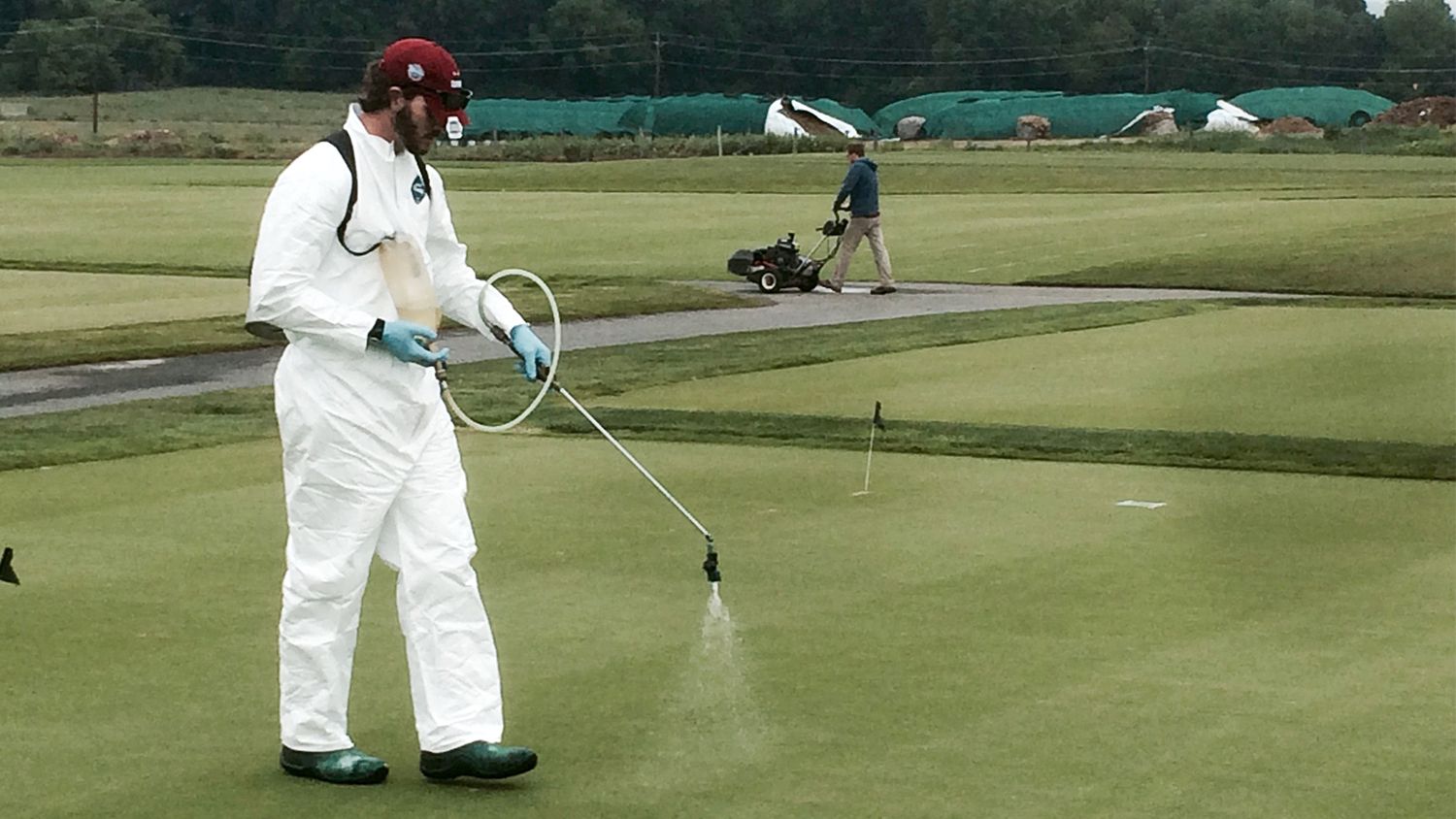 man in white protective suit sprays golf course green