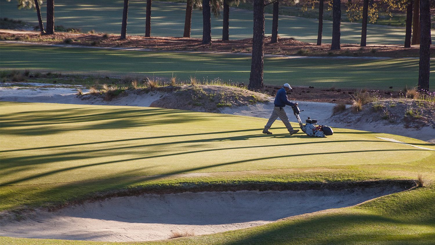 A maintenance worker mows a Pinehurst putting green.