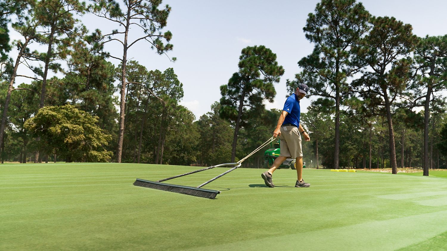 A golf course worker sweeps a putting green