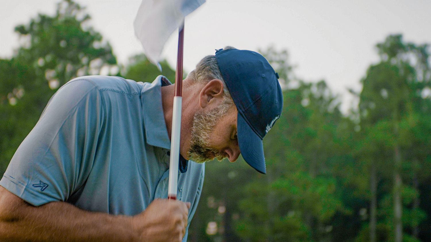 Man in a blue hat plants a golf hole flag