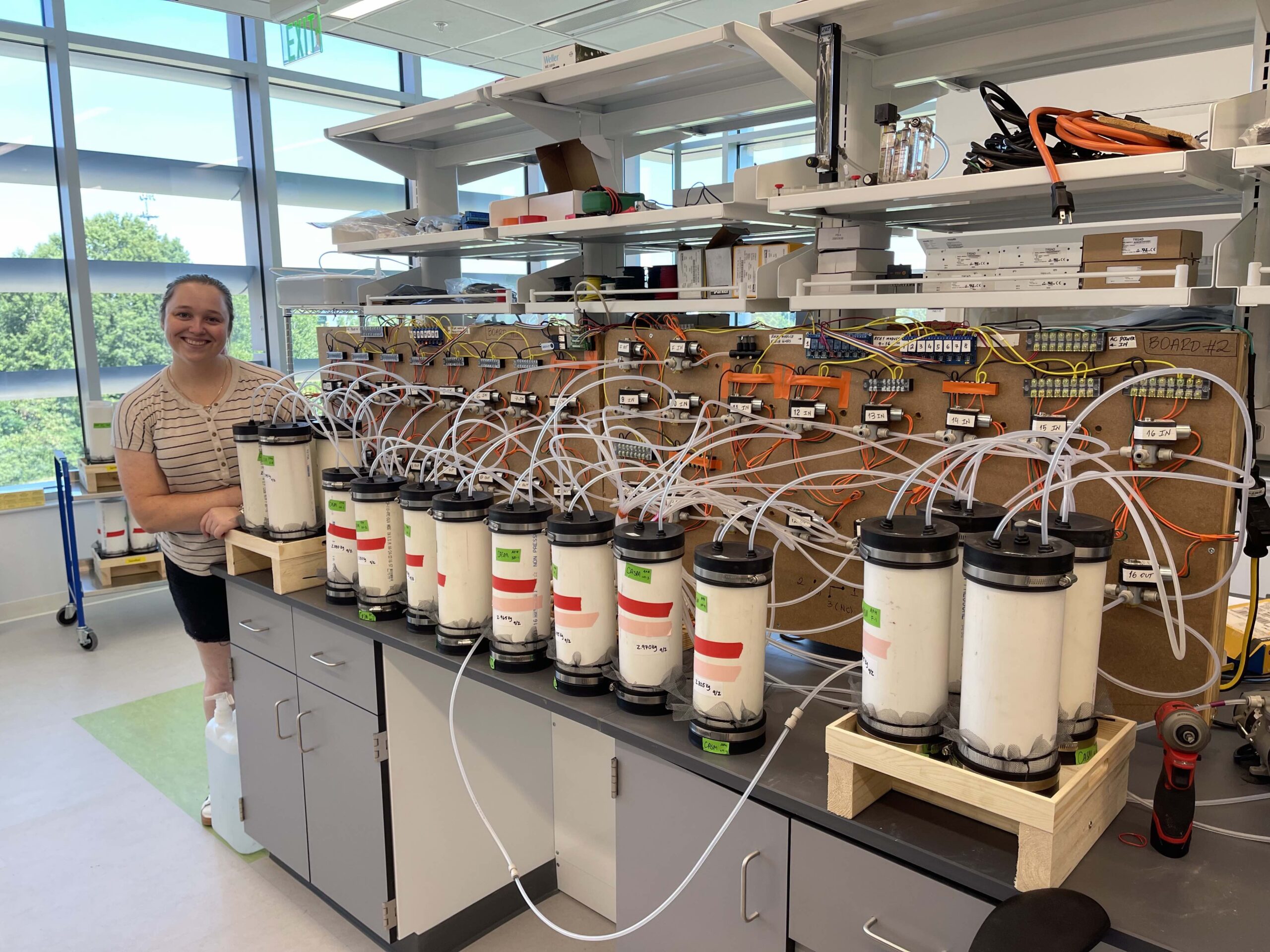 Julia Janson poses next to soil columns as part of her greenhouse gas measurements in flooded soil.