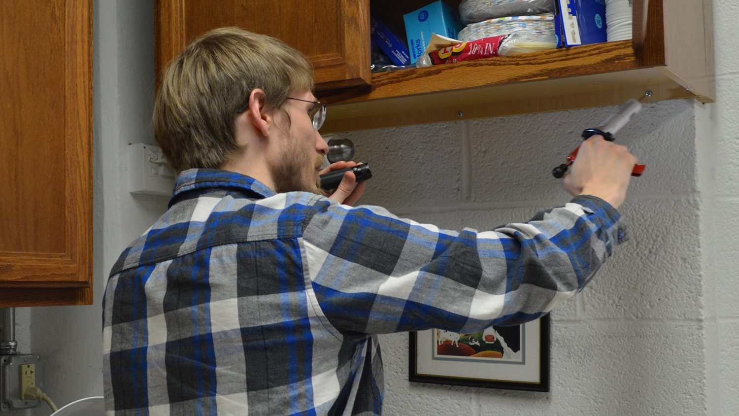 Photo of student applying a gel bait for cockroaches to a cabinet.
