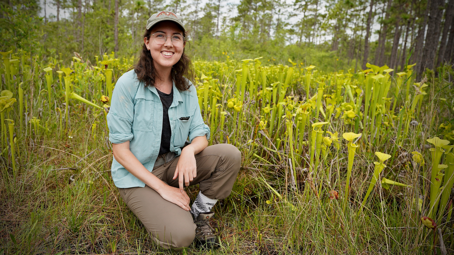 a female researcher sitting in a field smiling