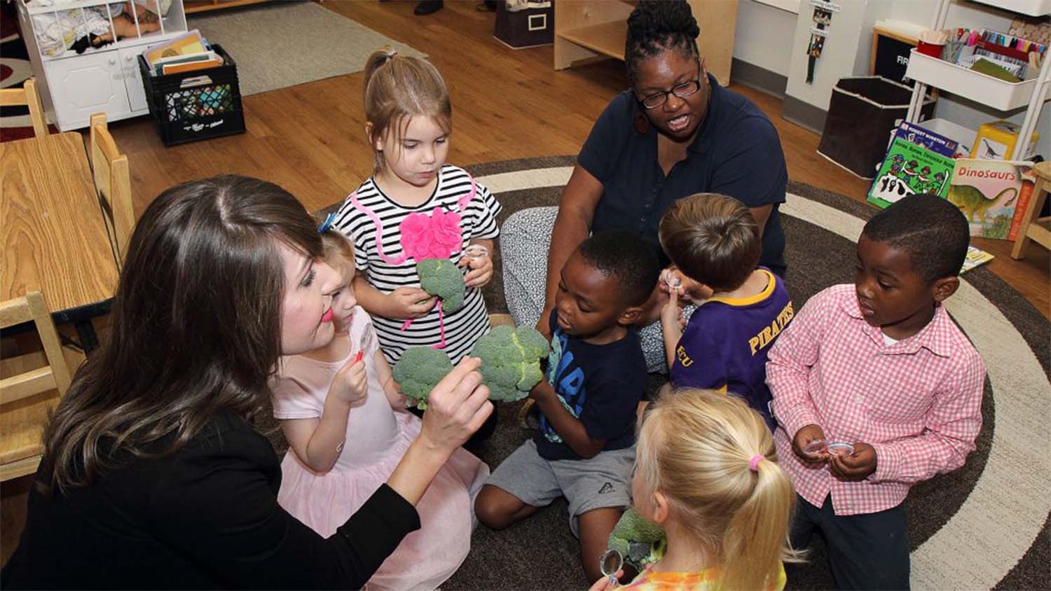 White woman showing broccoli to preschool children