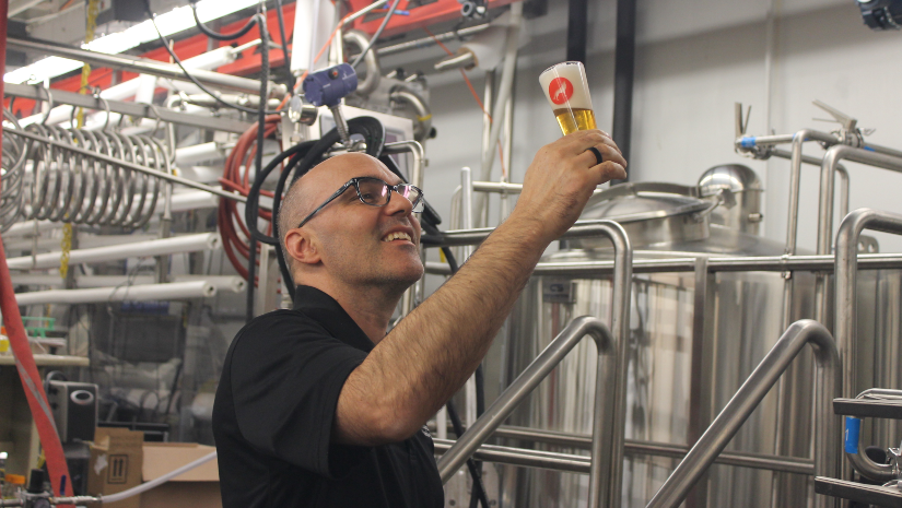 a man holding and inspecting a freshly brewed glass of beer