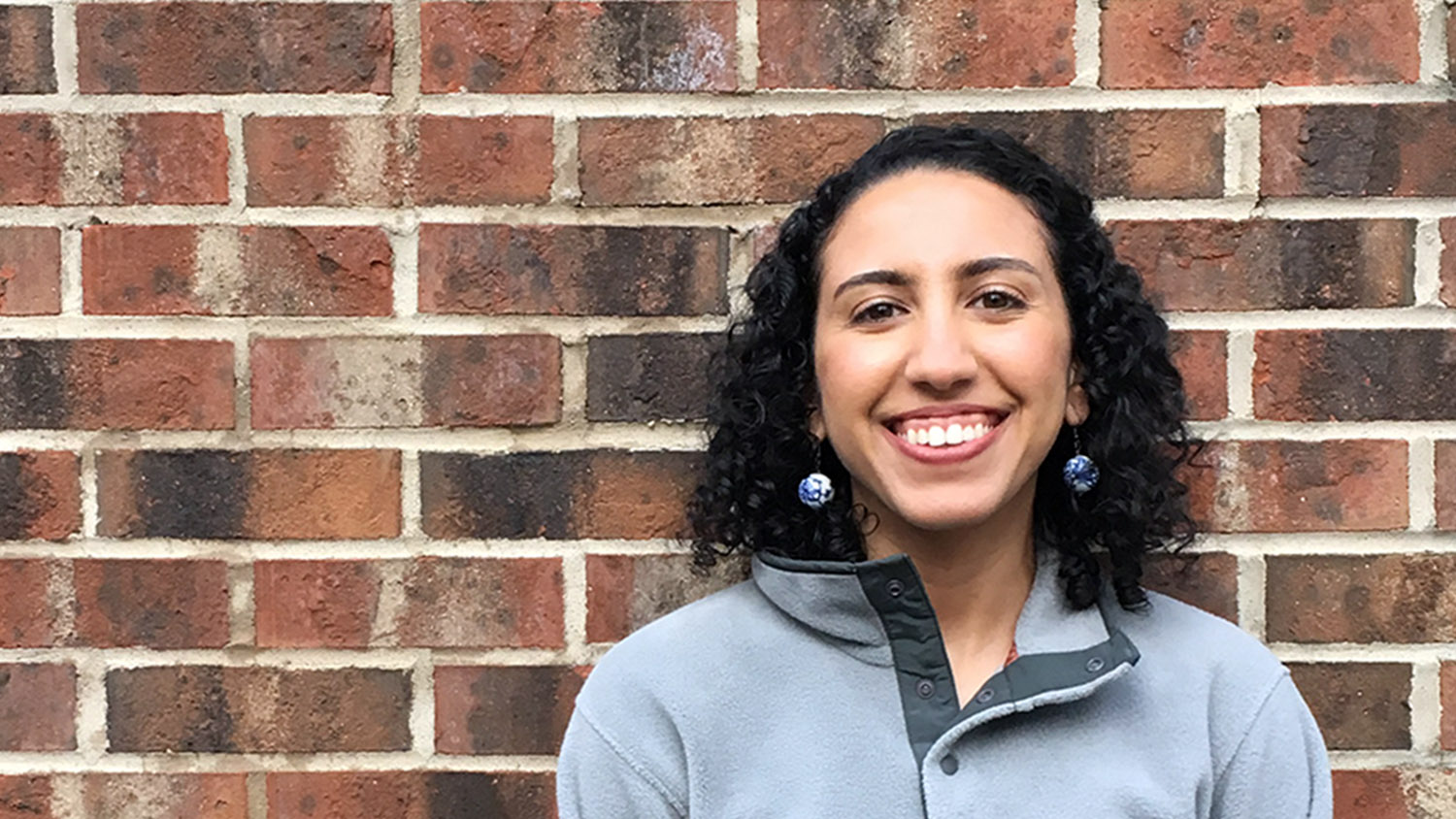 A smiling woman stands in front of a brick wall at the Horticultural Science department at NC State University's CALS.