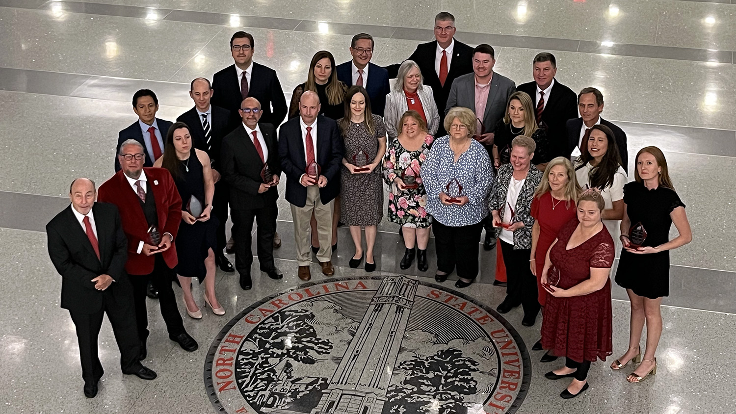 a group of people stand over the NC State university logo