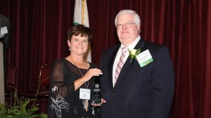 Man and woman standing on stage. Man is receiving an award.