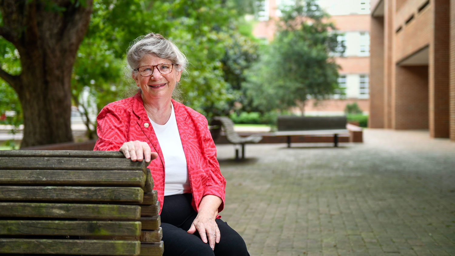 An older woman wearing glasses sitting on a bench