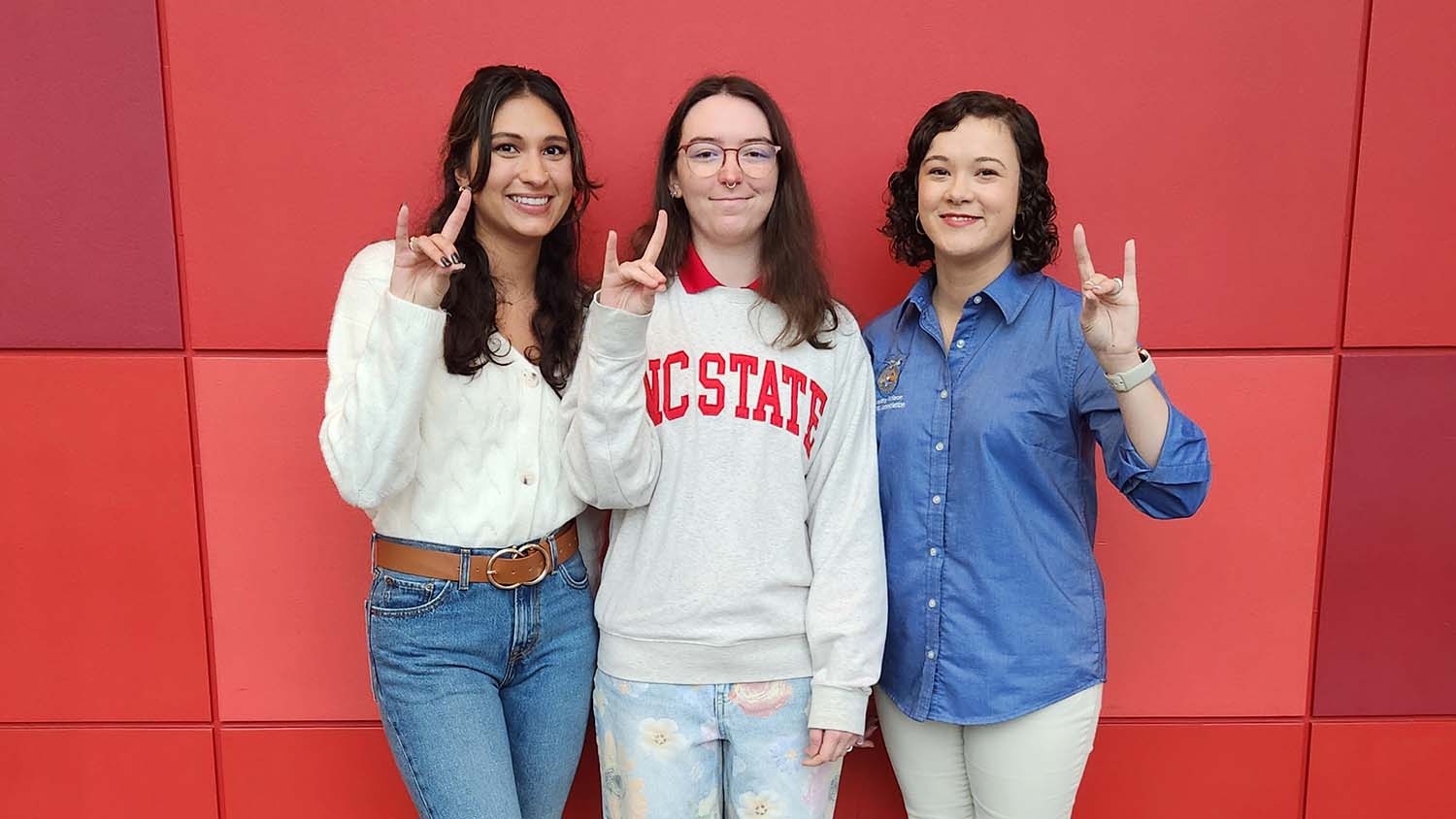 Three young woman posing in front of a red patterned wall