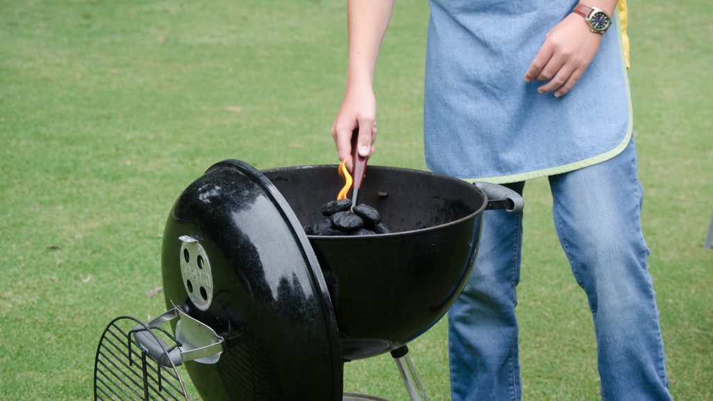 A griller lights charcoals in an outdoor grill