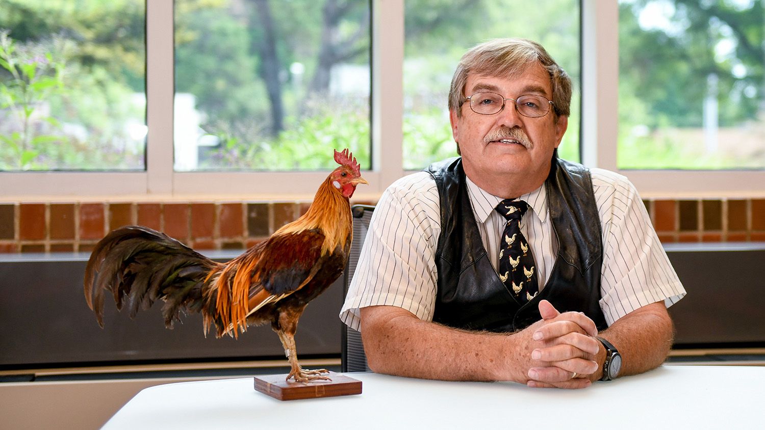 Man seated next to a taxidermy rooster.