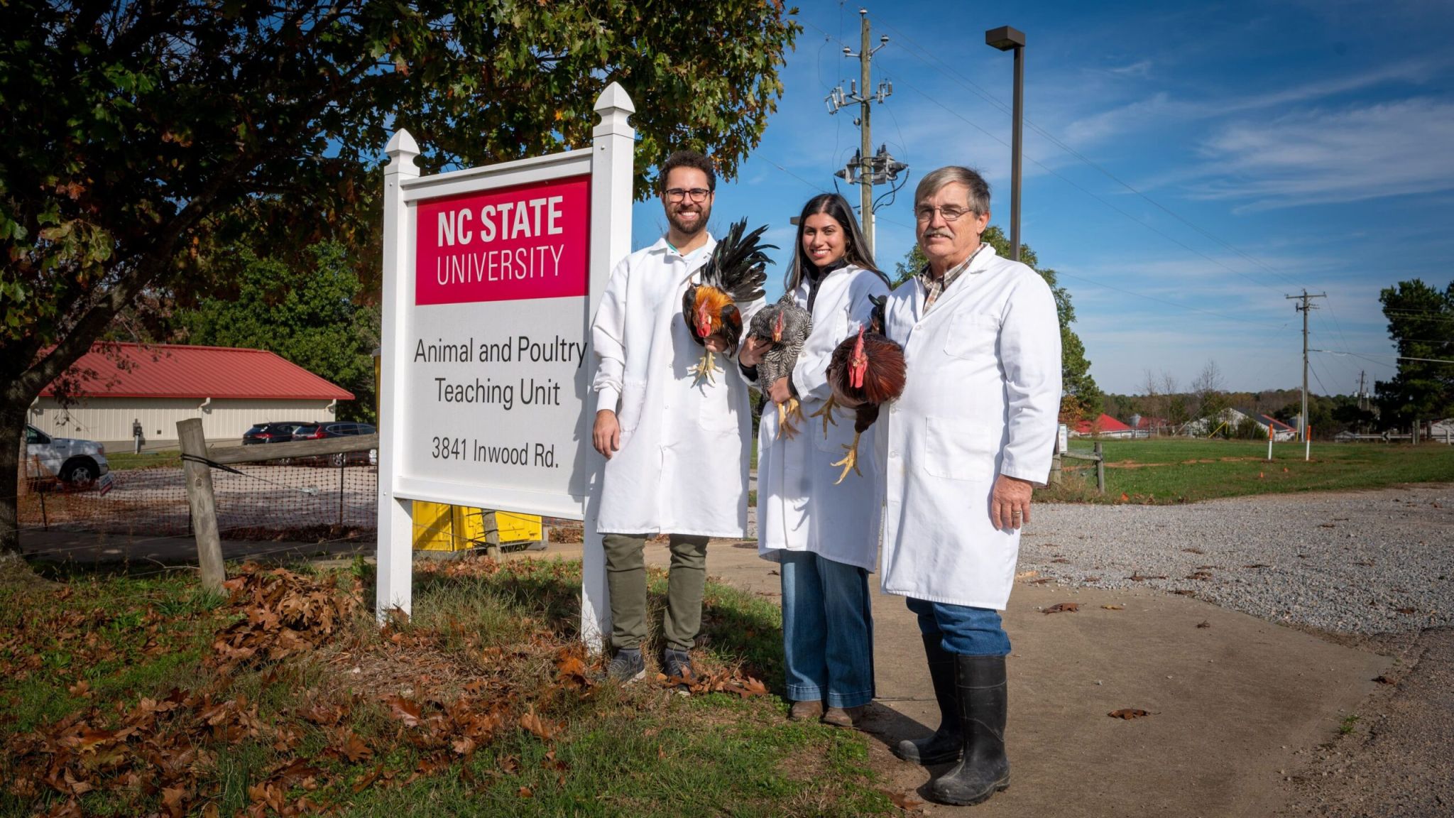 students and faculty standing in front of facility sign holding chickens