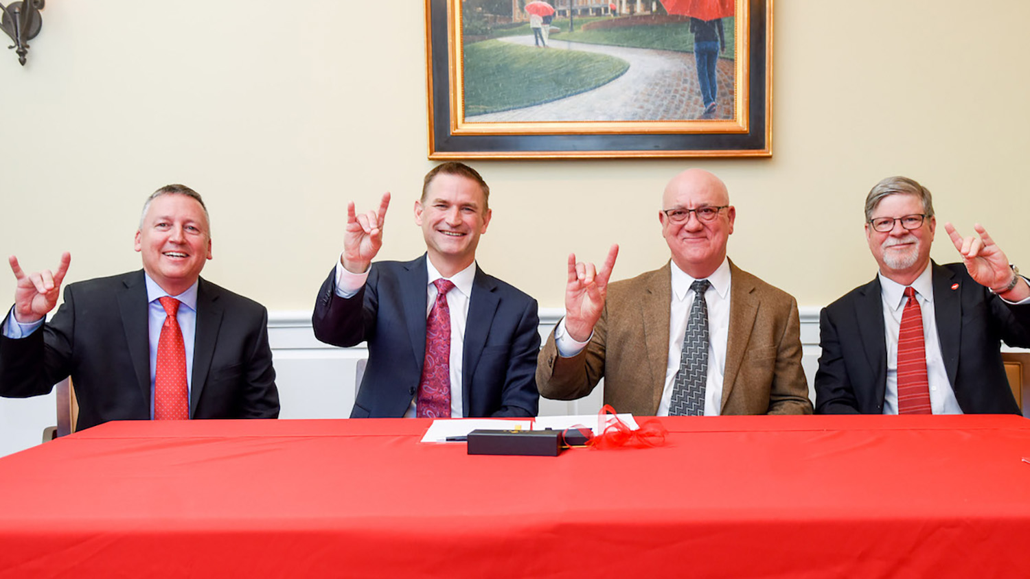 Four men at a red table give the wolf sign.