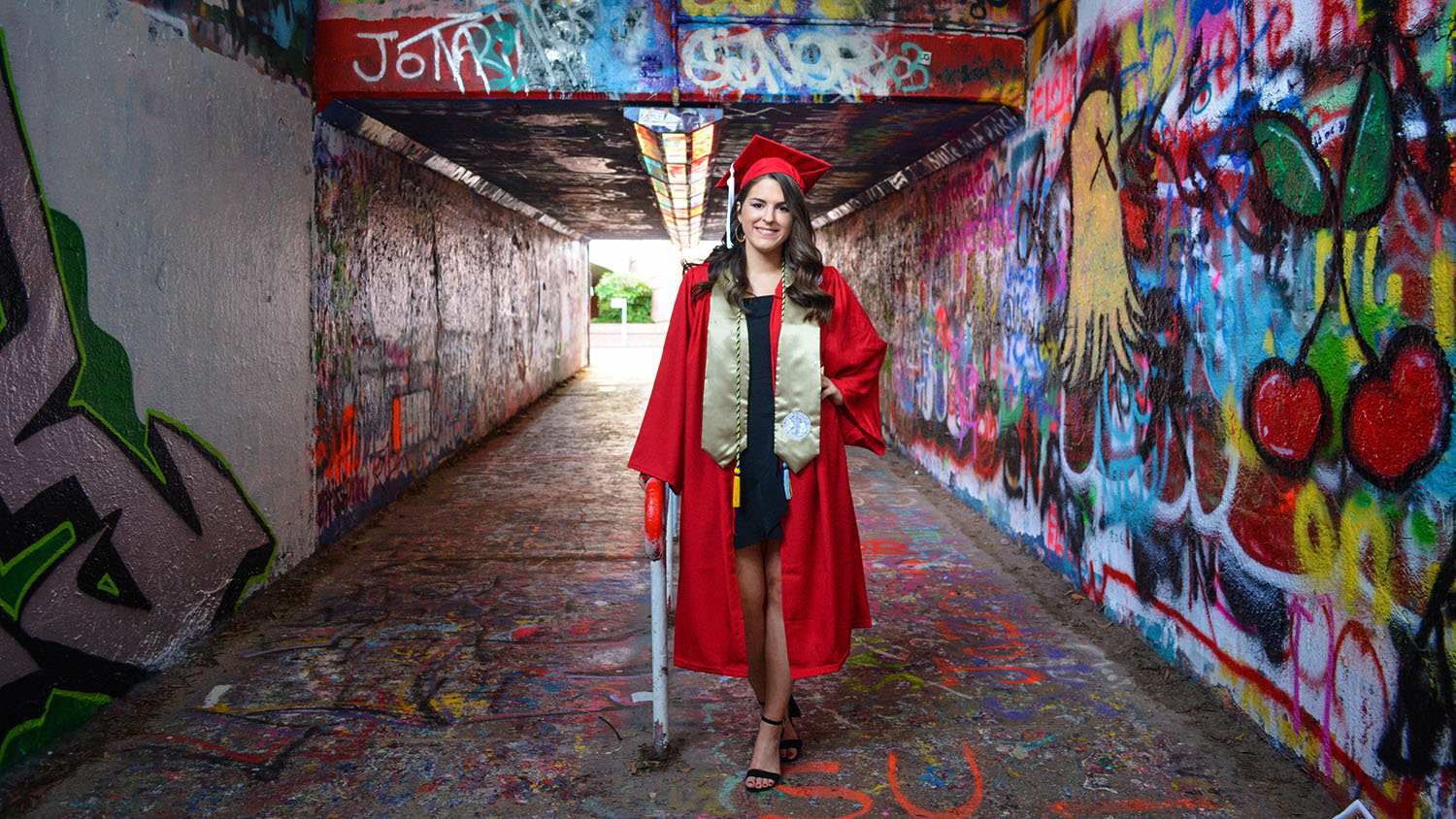 A CALS NC State graduate stands in the Free Expression Tunnel, framed by graffiti.