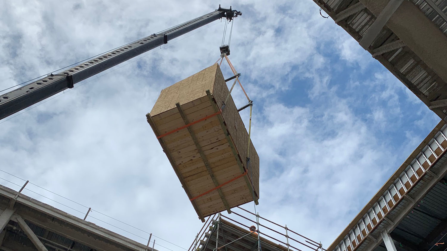 A wooden crate being hoisted by a crane into a building with a blue sky.