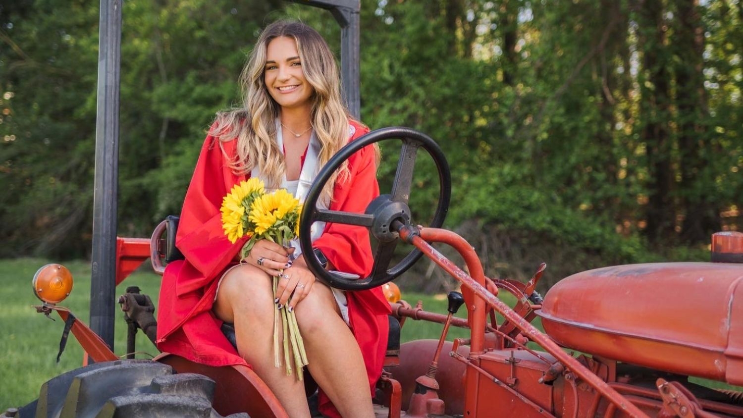 Abby Pleasant holding sunflowers in her graduation gown on a tractor