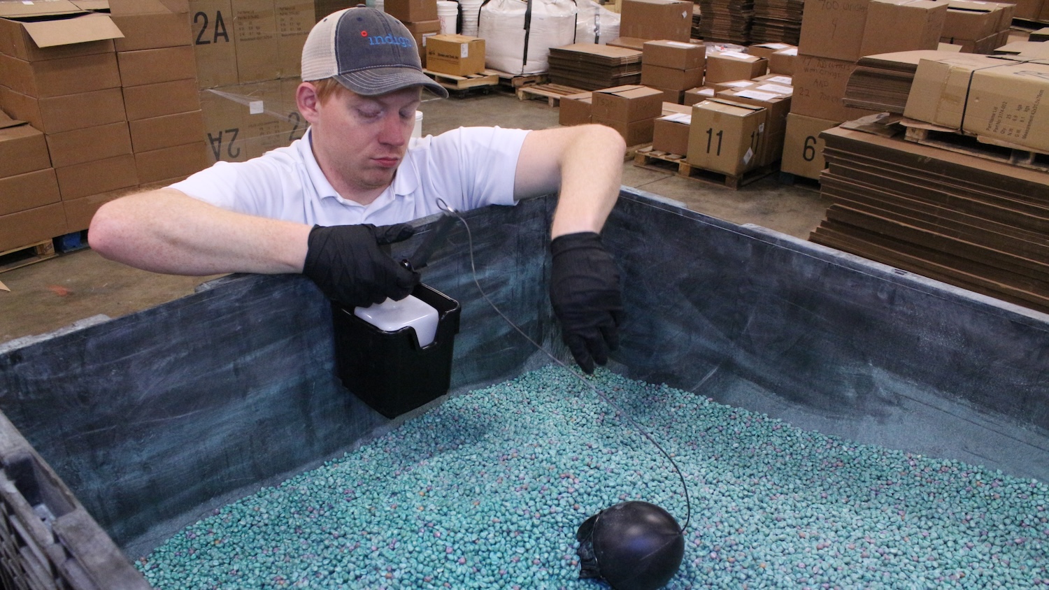 Man leaning over a box filled with small blue bead-like objects.