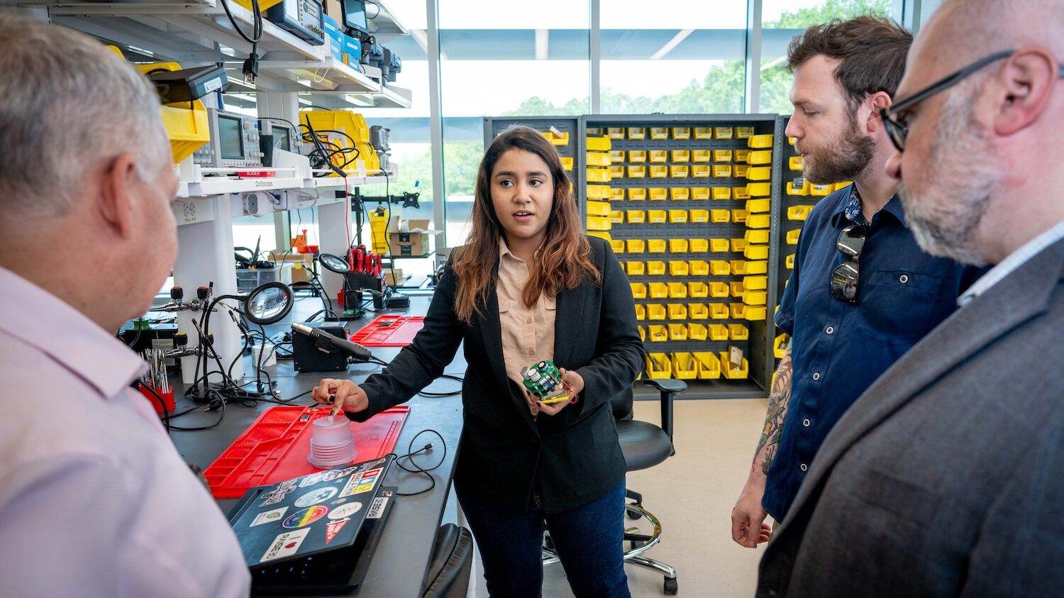 Woman holding an electronic sensor while three men look on.