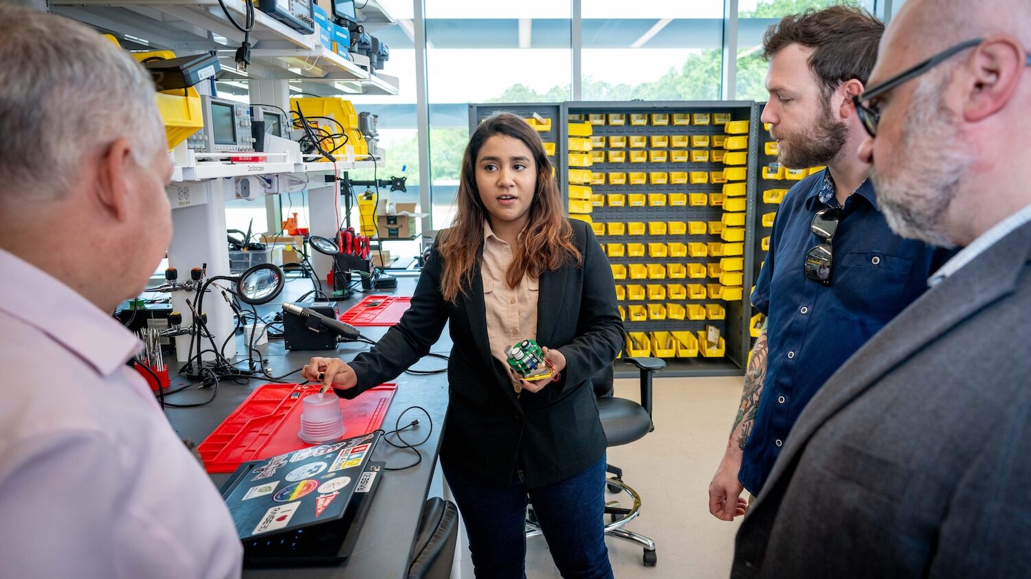 Woman holding an electronic sensor while three men look on.