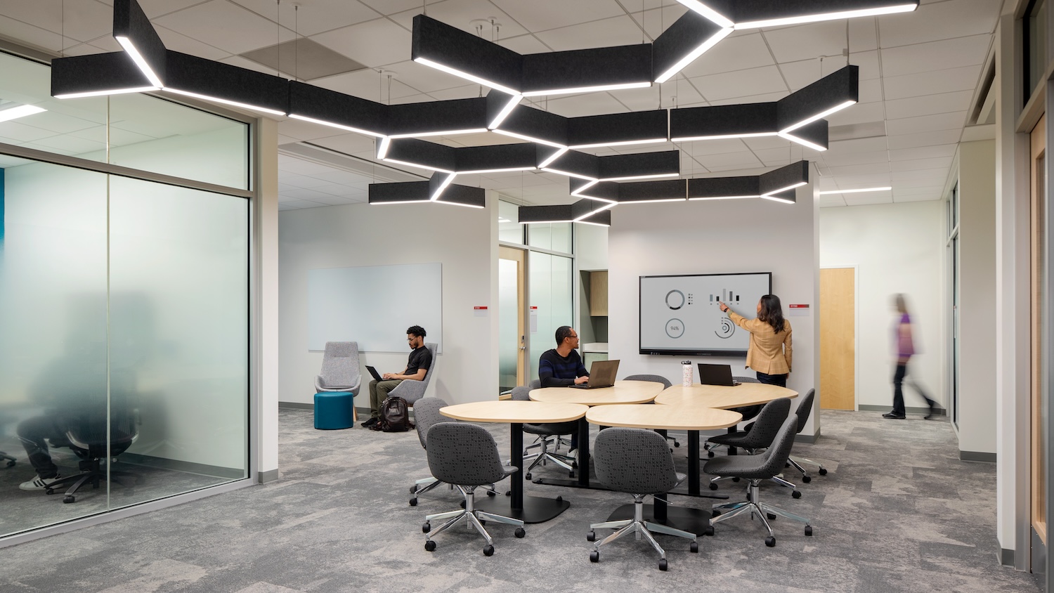 Several people in an open office space with whiteboard and tables and chairs.