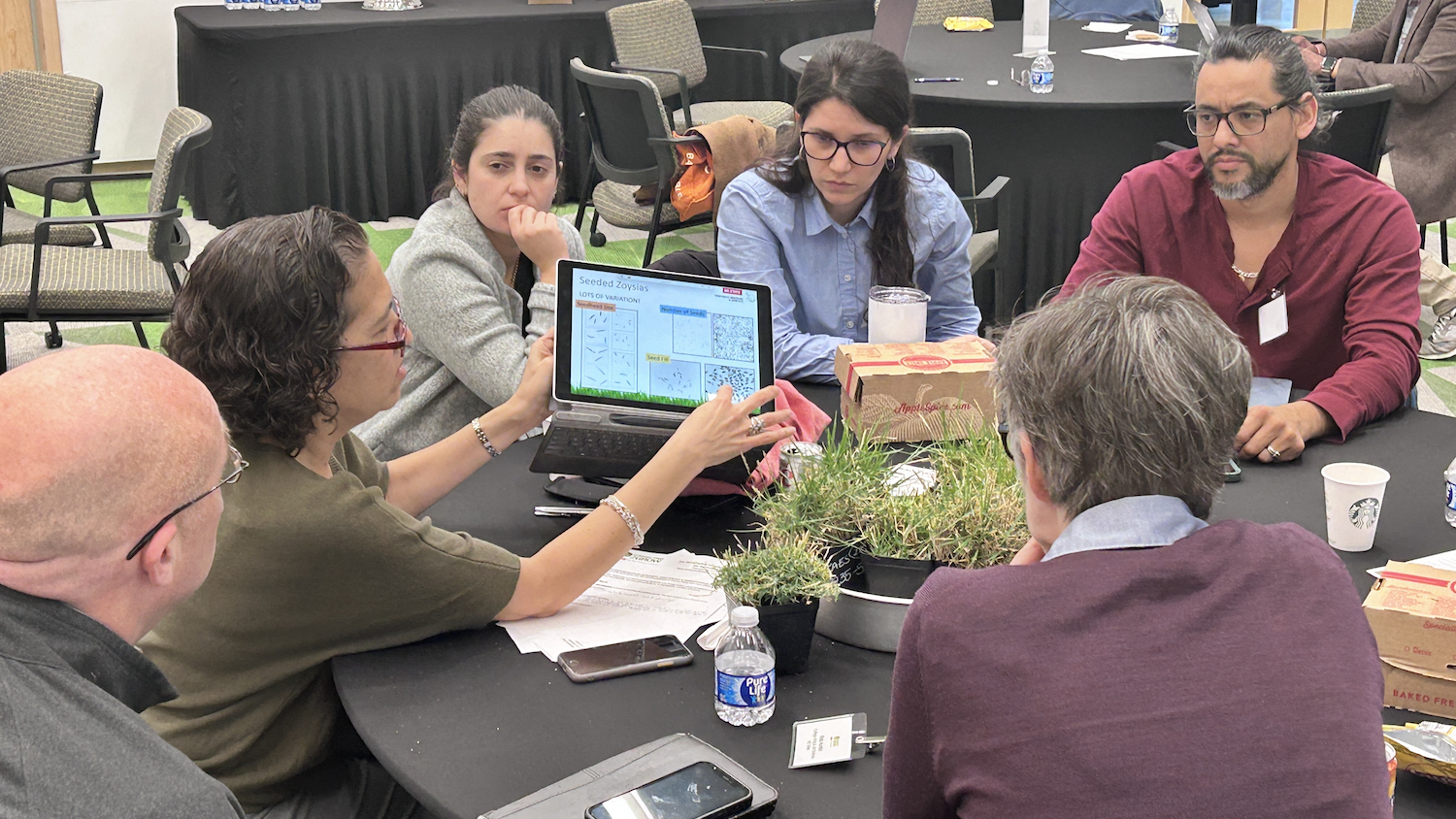 Group of scientists at a round table, with one holding up a computer tablet.