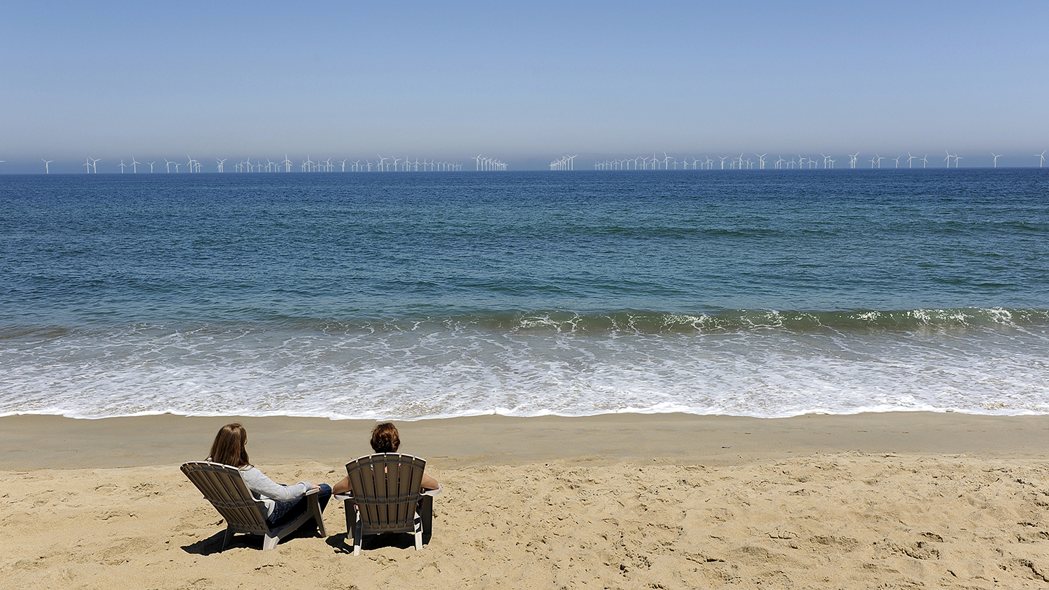 Two people on beach with wind farm in the distance.